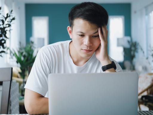 Ein junger Mann sitzt in die Arbeit versunken, den Kopf in eine Hand gestützt an seinem Laptop.